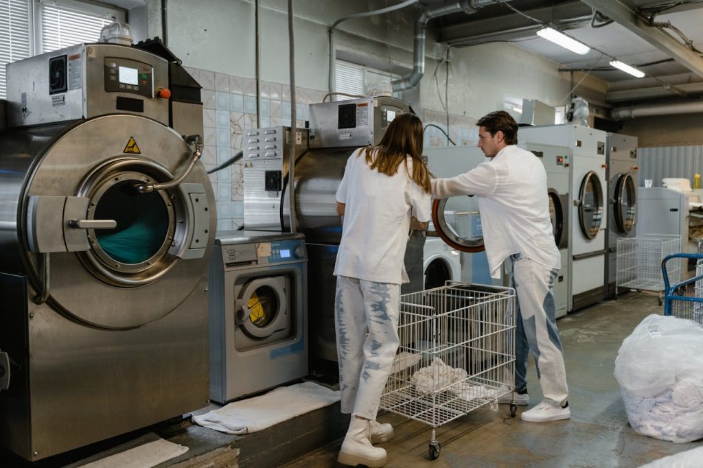 Two adults working in an industrial laundry facility with large machines.